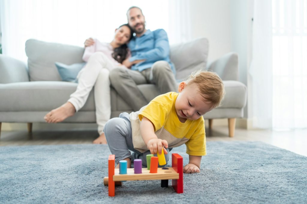 Caucasian loving parent looking at baby toddler playing in living room.